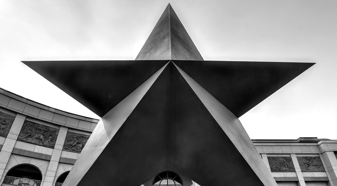Large metal star sculpture viewed from below, with a curved building in the background.