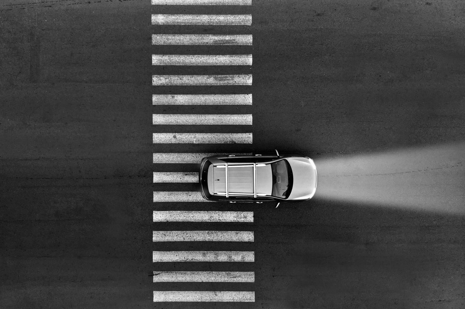 A car with its headlights on drives over a pedestrian crosswalk at night.
