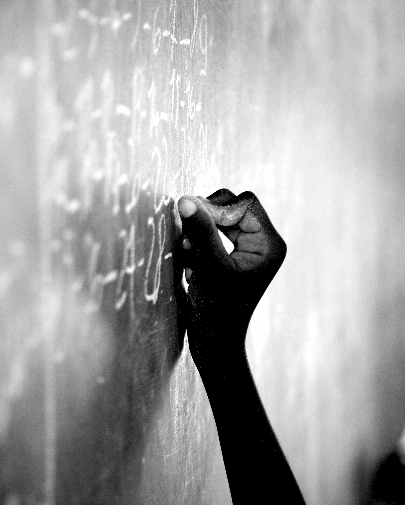 Hand writing mathematical equations on a chalkboard with chalk, shown in black and white.