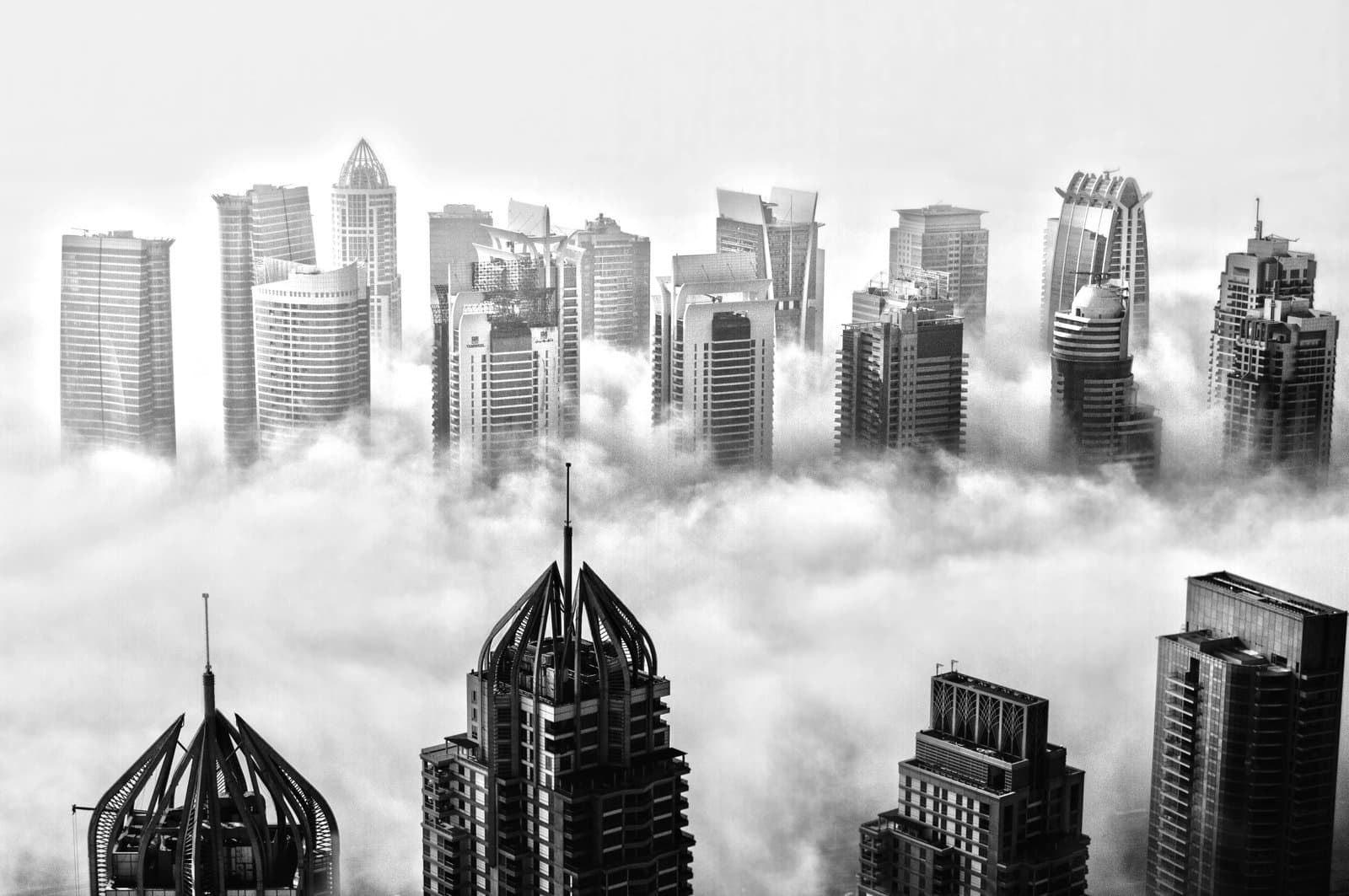 View of modern skyscrapers in Dubai emerging above thick clouds, with distinctive architectural designs and spires visible