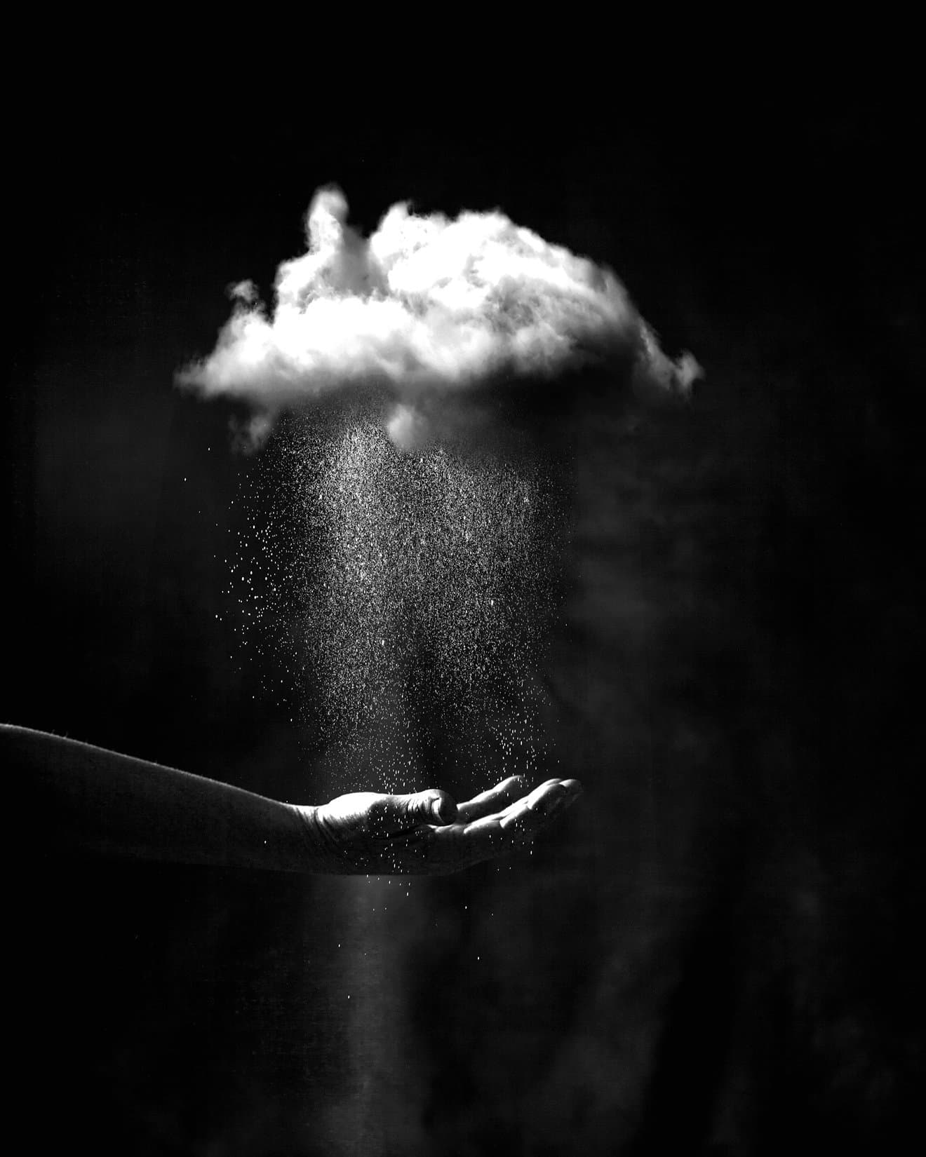 Hand held palm-up with fine particles falling onto it against a dark background in black and white.