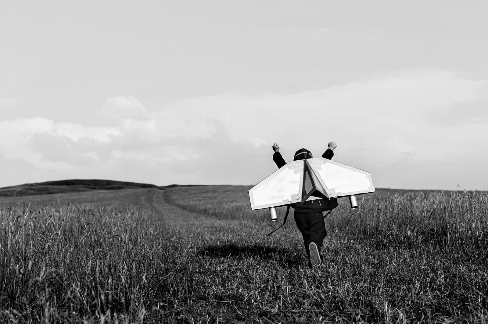 A young boy is wearing a jetpack running through a grass field 