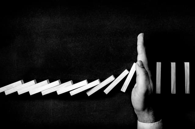 hand stopping dominoes toppling