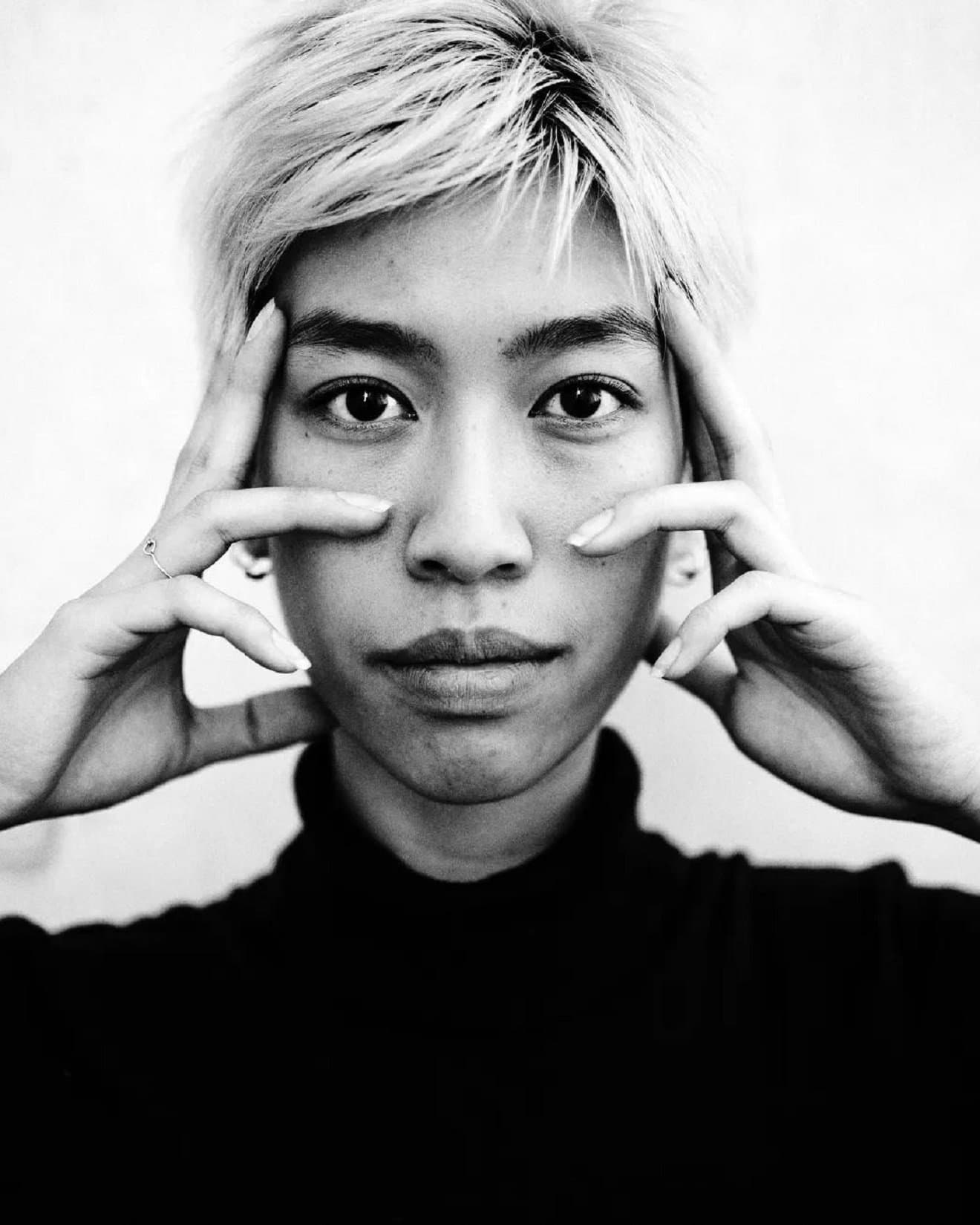 Woman with short hair holding her fingers against her temples and looking into the camera