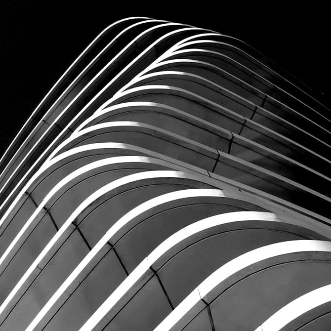 Curved modern building facade with repeating illuminated lines rising against a dark sky.