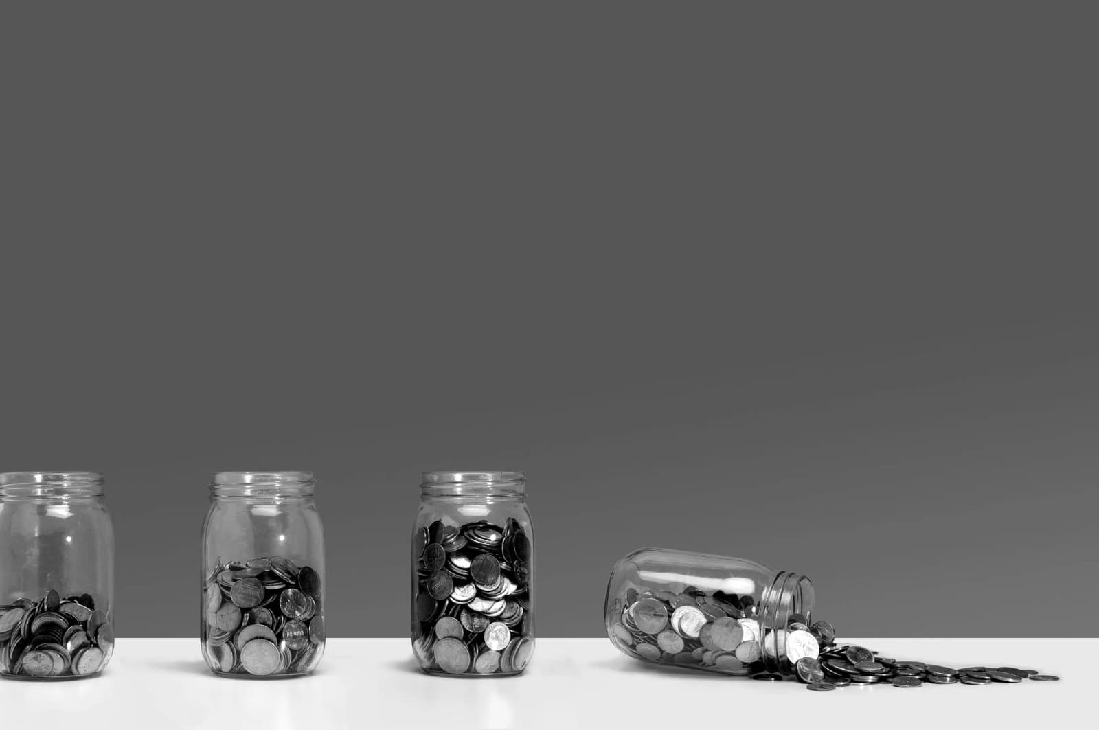Four jars of money, the furthest right jar toppled over, pouring the money out