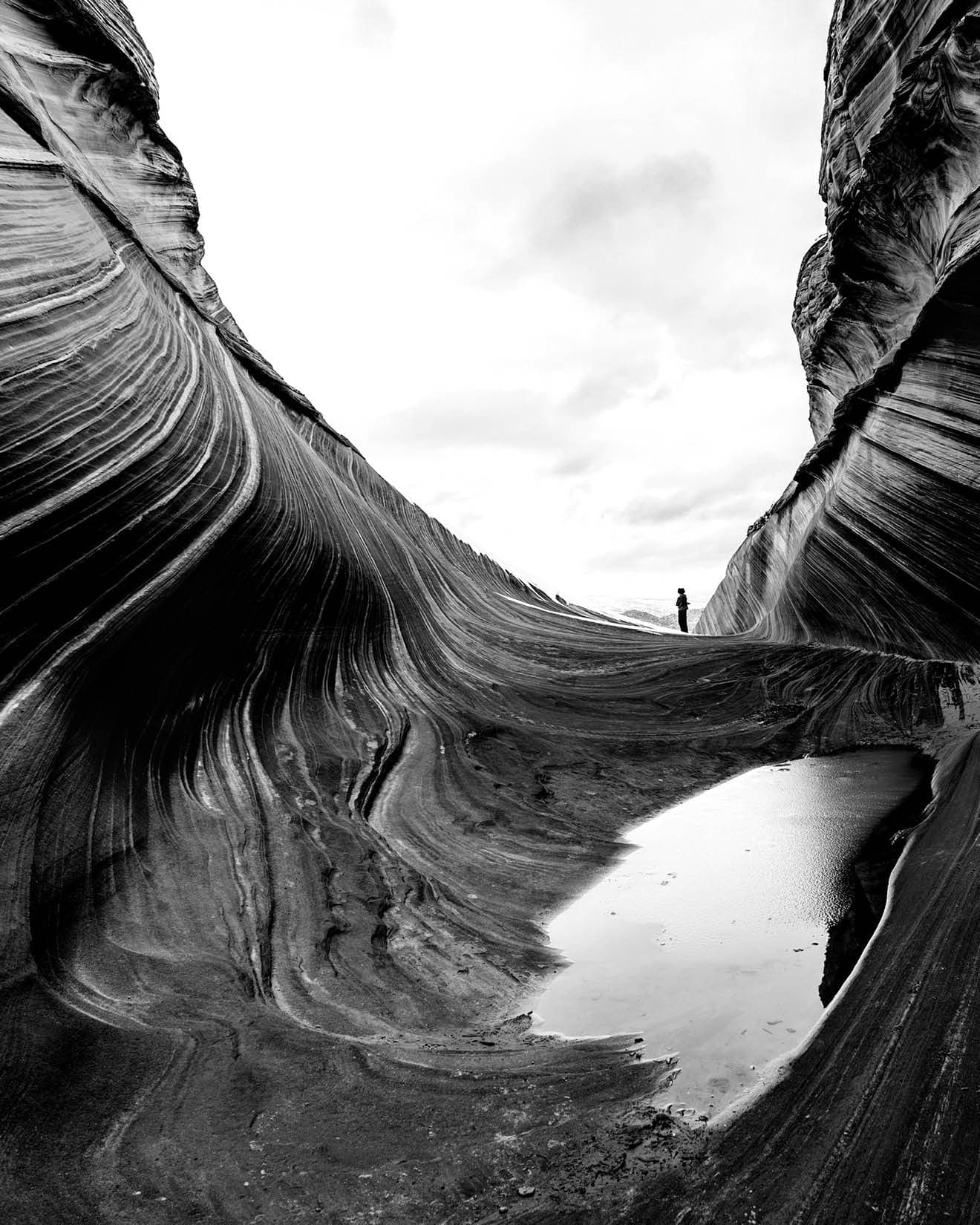 View of a winding sandstone canyon with a small person standing in the distance.