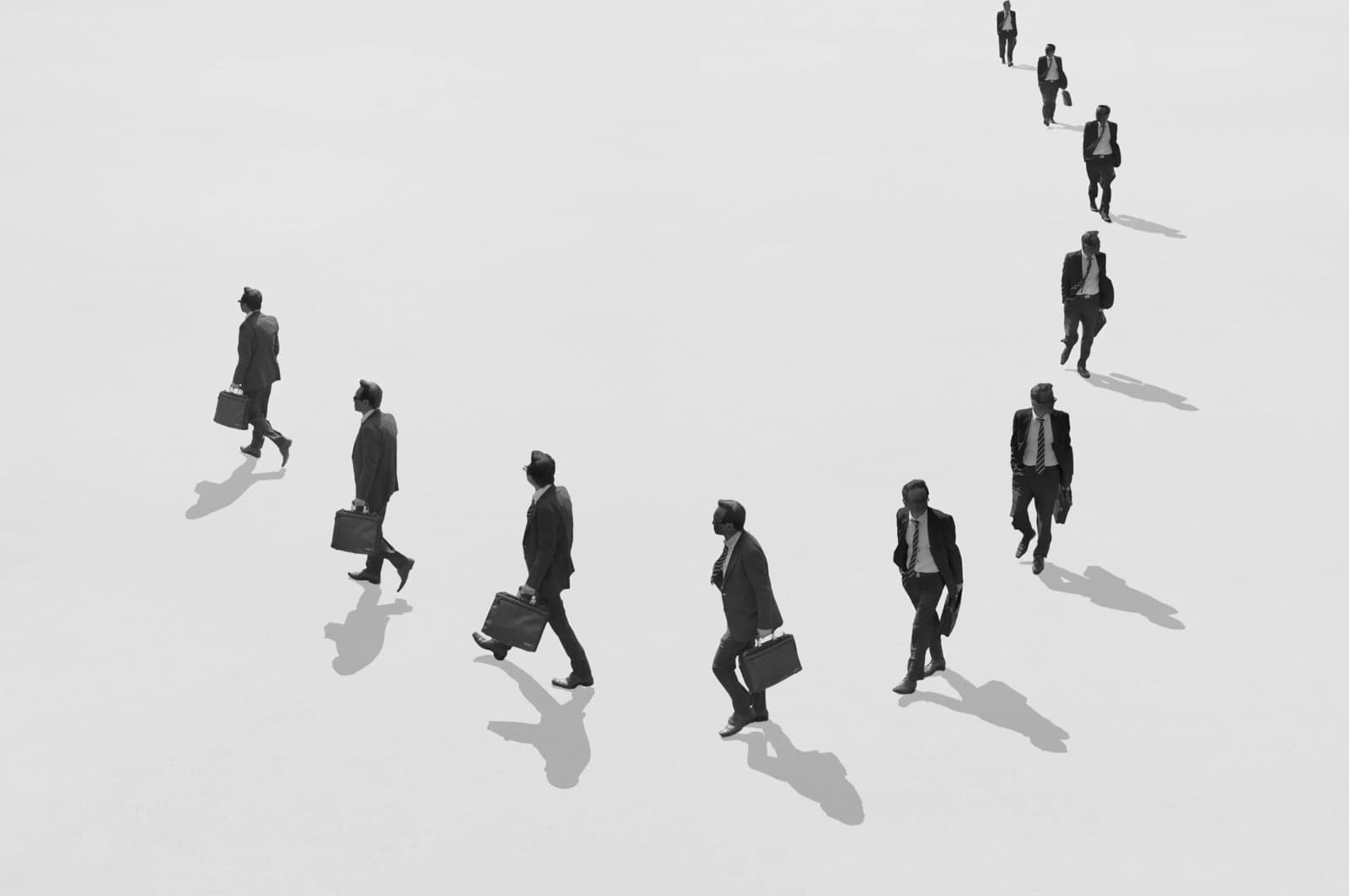 Ten people in business attire walking in a circular formation across an open space